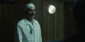 Movie still from “Chernobyl” (2019), directed by Johan Renck – A man in a white lab coat standing in front of a clock; Medium shot, Over the shoulder angle