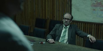 Movie still from “Chernobyl” (2019), directed by Johan Renck – A man sitting at a table in front of chairs; Medium shot, Over the shoulder angle