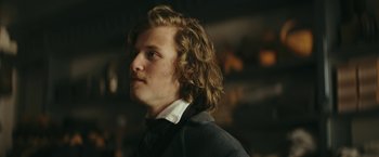 Movie still from “The Underground Railroad” (2021), directed by Barry Jenkins – A man with long hair and a white shirt is looking to his left; Close Up shot, Over the shoulder angle