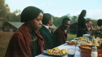 Movie still from “The Underground Railroad” (2021), directed by Barry Jenkins – A group of people sitting at a table with food on it; Medium shot, Over the shoulder angle