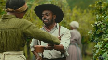 Movie still from “The Underground Railroad” (2021), directed by Barry Jenkins – A man holding a cup in his hands; Medium shot, Over the shoulder angle
