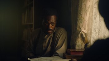 Movie still from “The Underground Railroad” (2021), directed by Barry Jenkins – A man sitting at a table in front of a book; Close Up shot, Over the shoulder angle