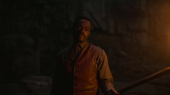 Movie still from “The Underground Railroad” (2021), directed by Barry Jenkins – A man holding a baseball bat while standing in the dark; Medium shot, Over the shoulder angle