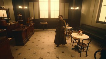 Movie still from “The Underground Railroad” (2021), directed by Barry Jenkins – A woman standing in a room with tables and chairs in front of a window; Extreme Wide shot, High angle