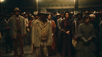 Movie still from “The Underground Railroad” (2021), directed by Barry Jenkins – A group of people standing around in a crowd of people; Wide shot, Over the shoulder angle