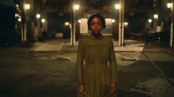 Movie still from “The Underground Railroad” (2021), directed by Barry Jenkins – A woman standing in front of a building at night; Medium shot, Low angle