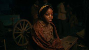 Movie still from “The Underground Railroad” (2021), directed by Barry Jenkins – A young girl wearing a yellow headscarf and a brown dress; Close Up shot, Over the shoulder angle