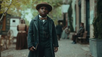 Movie still from “The Underground Railroad” (2021), directed by Barry Jenkins – A young boy dressed as a man in a long coat and hat; Close Up shot, High angle