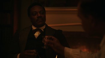 Movie still from “The Underground Railroad” (2021), directed by Barry Jenkins – A man wearing a suit and tie holding a glass; Close Up shot, Over the shoulder angle