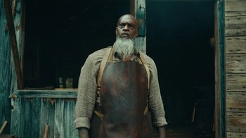 Movie still from “The Underground Railroad” (2021), directed by Barry Jenkins – A man wearing an apron standing in front of a building; Medium shot, Low angle