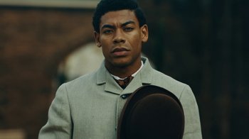 Movie still from “The Underground Railroad” (2021), directed by Barry Jenkins – A man wearing a suit and tie holding a hat; Close Up shot, Over the shoulder angle