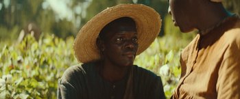 Movie still from “The Underground Railroad” (2021), directed by Barry Jenkins – A man wearing a straw hat in a field; Close Up shot, Low angle