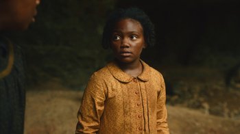 Movie still from “The Underground Railroad” (2021), directed by Barry Jenkins – A young girl in a yellow dress is standing outside; Close Up shot, High angle