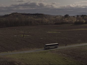 Movie still from “The Whale” (2022), directed by Darren Aronofsky – A bus driving down a road near a field; Extreme Wide shot, High angle