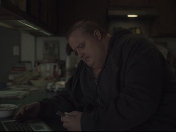Movie still from “The Whale” (2022), directed by Darren Aronofsky – A man in a black jacket is looking at a cell phone; Medium shot, High angle