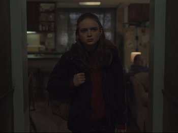 Movie still from “The Whale” (2022), directed by Darren Aronofsky – A young woman standing in a dark room holding a purse; Medium shot, Over the shoulder angle