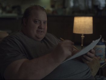 Movie still from “The Whale” (2022), directed by Darren Aronofsky – A man sitting on a couch writing on a piece of paper; Close Up shot, Low angle