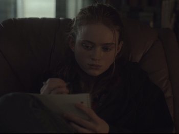 Movie still from “The Whale” (2022), directed by Darren Aronofsky – A woman sitting on a couch writing on a piece of paper; Close Up shot, Over the shoulder angle