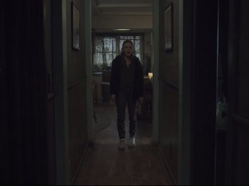 Movie still from “The Whale” (2022), directed by Darren Aronofsky – A man standing in a hallway with a light on; Wide shot, Low angle