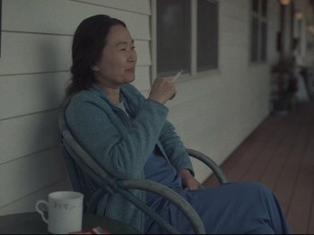 Movie still from “The Whale” (2022), directed by Darren Aronofsky – A woman sitting in a chair on a porch; Medium shot, Low angle