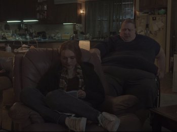 Movie still from “The Whale” (2022), directed by Darren Aronofsky – A man and a woman sitting on a couch in a living room; Medium shot, Over the shoulder angle