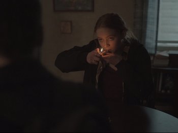 Movie still from “The Whale” (2022), directed by Darren Aronofsky – A young girl lighting a cigarette in a dark room; Medium shot, Over the shoulder angle