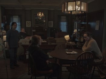 Movie still from “The Whale” (2022), directed by Darren Aronofsky – A group of people sitting around a table in a room; Wide shot, High angle
