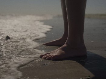Movie still from “The Whale” (2022), directed by Darren Aronofsky – A person standing on a beach with their feet in the water; Extreme Close Up shot, Low angle