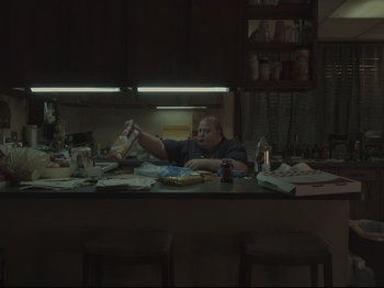 Movie still from “The Whale” (2022), directed by Darren Aronofsky – A man sitting at a kitchen table eating food; Wide shot, High angle