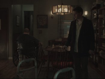Movie still from “The Whale” (2022), directed by Darren Aronofsky – A man standing next to a man sitting at a table; Wide shot, Over the shoulder angle