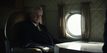 Movie still from “Chernobyl” (2019), directed by Johan Renck – An older man in a suit sitting in front of an airplane window; Medium shot, Low angle