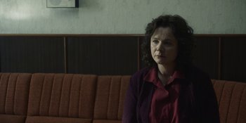 Movie still from “Chernobyl” (2019), directed by Johan Renck – A woman sitting on a couch in front of a window; Medium shot, Over the shoulder angle