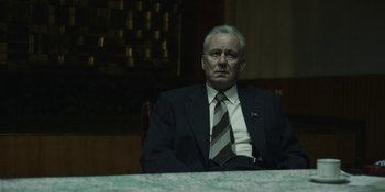 Movie still from “Chernobyl” (2019), directed by Johan Renck – An older man in a suit and tie sitting at a table; Medium shot, Low angle