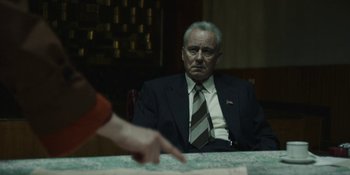 Movie still from “Chernobyl” (2019), directed by Johan Renck – An older man sitting at a table with a hand pointing at him; Medium shot, Over the shoulder angle