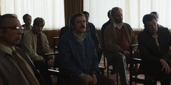 Movie still from “Chernobyl” (2019), directed by Johan Renck – A group of men sitting in a room listening intently; Medium shot, High angle