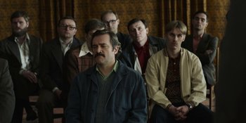 Movie still from “Chernobyl” (2019), directed by Johan Renck – A group of men standing next to each other in front of a wall; Medium shot, High angle