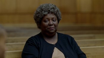 Movie still from “The Wire” (2002), created by David Simon – An older black woman sitting in front of a wooden wall; Close Up shot, Over the shoulder angle
