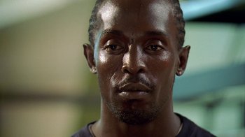 Movie still from “The Wire” (2002), created by David Simon – A man's face in a black shirt; Close Up shot, Low angle