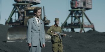 Movie still from “Chernobyl” (2019), directed by Johan Renck – A man in a suit and a man with a gun in his hand; Medium shot, Over the shoulder angle