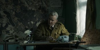 Movie still from “Chernobyl” (2019), directed by Johan Renck – An older man sitting at a table in a room; Medium shot, High angle