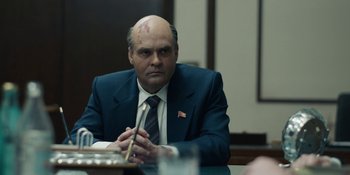 Movie still from “Chernobyl” (2019), directed by Johan Renck – A man with a bald head sitting at a table; Medium shot, Over the shoulder angle