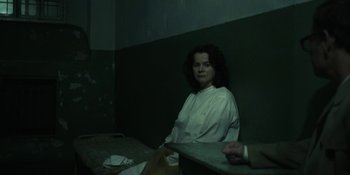 Movie still from “Chernobyl” (2019), directed by Johan Renck – A woman sitting in a dark room next to a wall; Medium shot, Over the shoulder angle