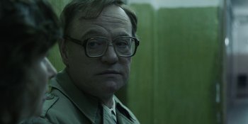 Movie still from “Chernobyl” (2019), directed by Johan Renck – An older man wearing glasses looking at the camera; Close Up shot, Over the shoulder angle