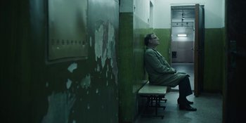 Movie still from “Chernobyl” (2019), directed by Johan Renck – A man sitting on top of a bench in a jail cell; Medium shot, High angle