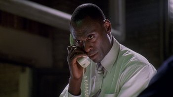 Movie still from “The Wire” (2002), created by David Simon – A man talking on a phone while sitting down; Close Up shot, Low angle