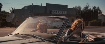 Movie still from “Thelma & Louise” (1991), directed by Ridley Scott – Two women in a car with a market in the background; Wide shot, Over the shoulder angle