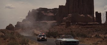 Movie still from “Thelma & Louise” (1991), directed by Ridley Scott – Two cars driving down a road in the middle of the desert; Extreme Wide shot, Over the shoulder angle
