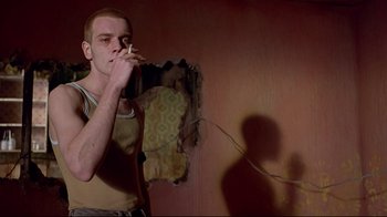 Movie still from “Trainspotting” (1996), directed by Danny Boyle – A man smoking a cigarette in a room; Medium shot, Low angle
