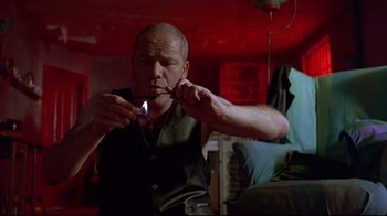 Movie still from “Trainspotting” (1996), directed by Danny Boyle – A man lighting a cigarette in a room with red walls; Medium shot, Low angle