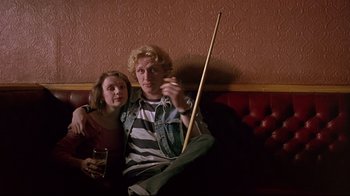 Movie still from “Trainspotting” (1996), directed by Danny Boyle – A man and a woman sitting on a couch holding a pool cue; Medium shot, Low angle